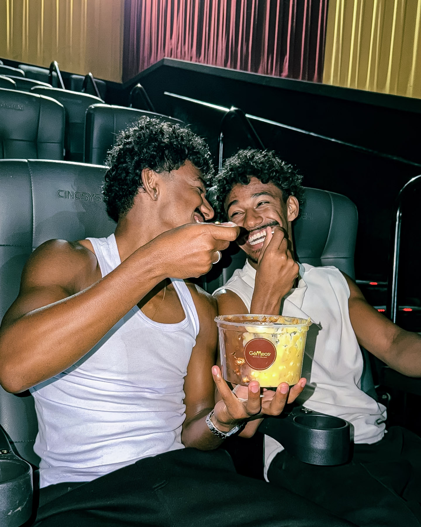 Victor e Vinícius rindo no cinema dividindo um balde de pipoca gourmet Gêmeos